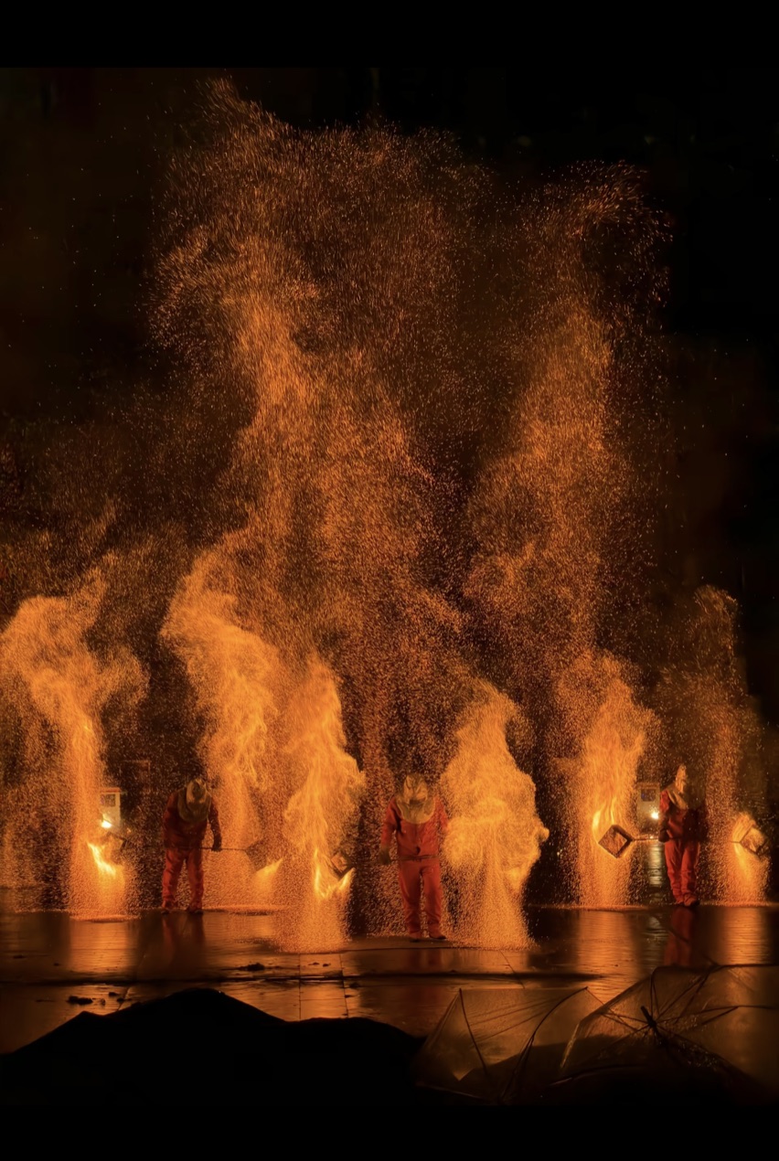 Performers silhouetted against a burst of molten iron sparks at a nighttime Chinese folk fireworks show